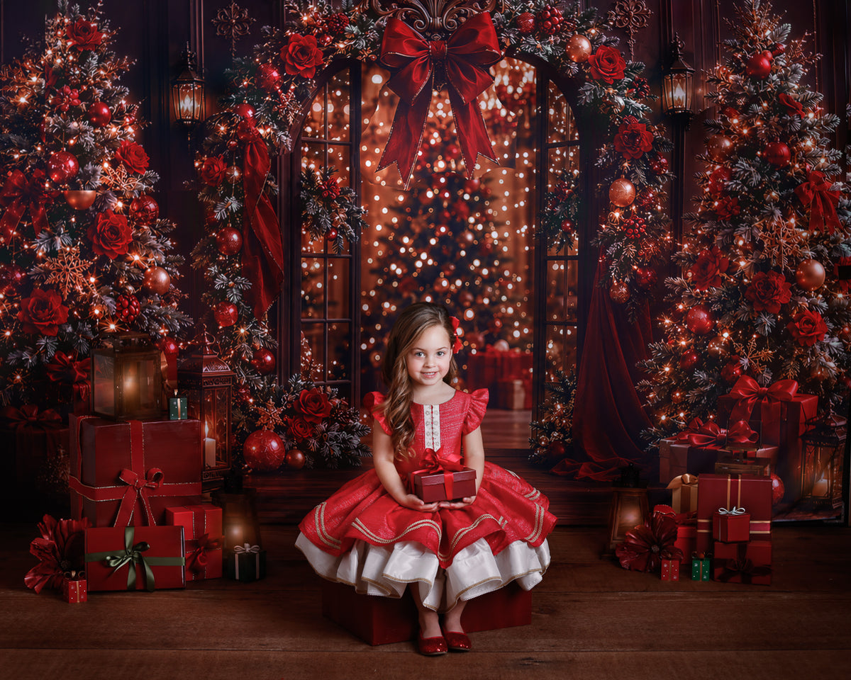 Christmas mini session at Melissa Larson's Perth studio: a young girl in a red and white holiday dress sits on a gift box among Christmas trees, presents and warm string lights